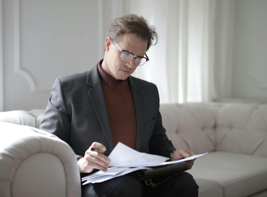 pexels-photo-3760514-3760514 Elegant adult man in jacket and glasses looking through documents while sitting on white sofa in luxury room