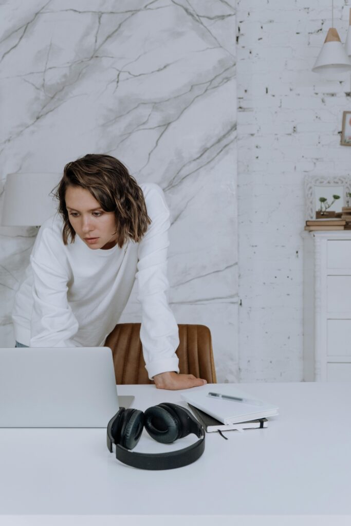 pexels-photo-5081389-5081389 A woman in a white sweater focuses on work at her laptop in a stylish home office setting.